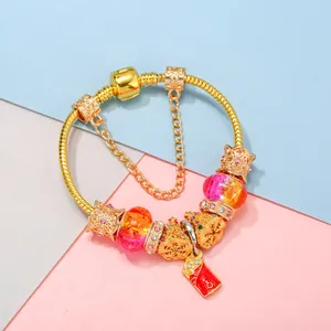Golden snake chain bracelet with festive charms and gradient glass beads on pink background