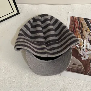 Close-up of grey striped knit visor hat with ear protection on a minimalist background
