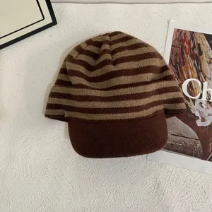 Detail showing thick striped knit beanie with visor in warm brown and beige tones