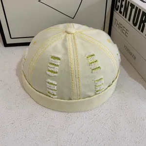 Dettaglio macro del cappello docker in tela beige con cuciture gialle a contrasto e strappi