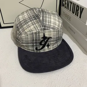 Detail of retro plaid camper hat with embroidered logo and wool brim on book stack