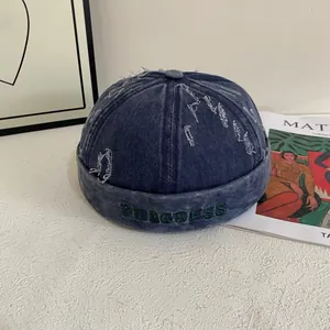 Detail of blue denim docker hat featuring distressed holes and green Progress embroidery