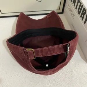 Detail view of burgundy baseball cap showing metal buckle and textured cotton fabric