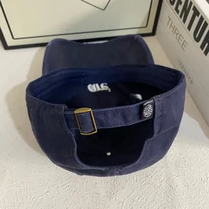 Detail view of deep blue baseball cap with adjustable metal buckle and woven brand label