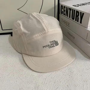 Detalle de gorra beige de cinco paneles de secado rápido con logotipo The Peek and Trail