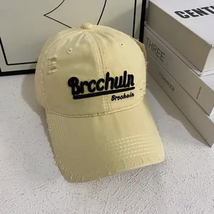 Dettaglio del cappellino beige consumato con ricamo di lettere nere sulla corona