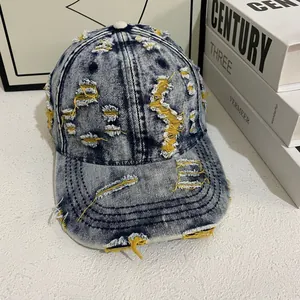 Detail of distressed denim baseball cap with frayed holes and yellow stitching accents
