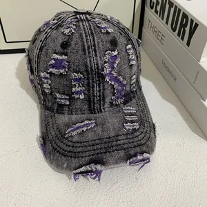 Close-up of distressed denim baseball cap with torn details and purple inner fibers