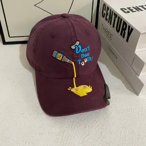 Detail of burgundy baseball cap with blue embroidery and metal bottle opener on brim