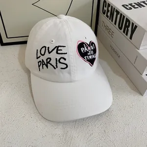 Detalle del bordado LOVE PARIS y parche de corazón en gorra de béisbol blanca