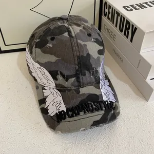 Detailed embroidery of white angel wings on a distressed camouflage baseball cap