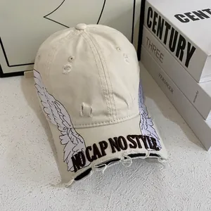 Detail of wing embroidery and distressed brim on cream cotton baseball cap