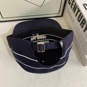 Detail of navy blue cotton cap featuring metal buckle and white stripe embroidery