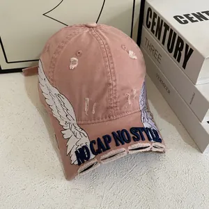 Close-up of pink baseball cap featuring white wing embroidery and distressed brim details