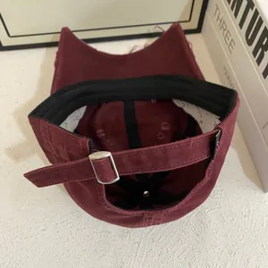 Detail of burgundy cotton baseball cap showing internal stitching and adjustable metal buckle
