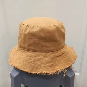 Détail du bord effiloché d'un chapeau bob en toile moutarde avec garniture à franges