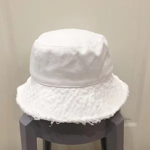 Détail d'un chapeau bob en toile blanche avec bords effilochés et finitions frangées
