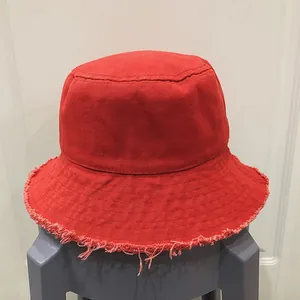 Gros plan détaillé du chapeau bob en toile rouge montrant le bord effiloché au fini brut