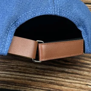 Détail de la casquette en denim bleu avec sangle réglable en cuir marron et boucle métal