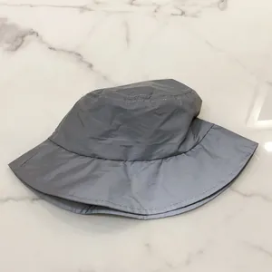 Top view of a grey reflective nylon bucket hat on a white marble surface with visible stitching
