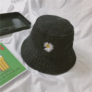 Black denim bucket hat with daisy embroidery on white fabric with minimalist props