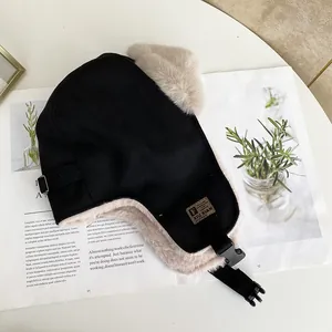 Dettaglio del cappello da aviatore nero con fodera in ecopelliccia beige e fibbia su tavolo