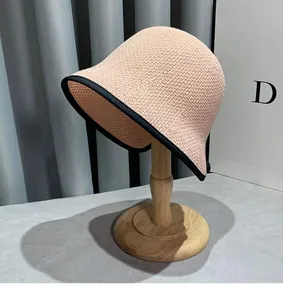 Detail of light pink woven bucket hat with black contrast trim on a wooden stand