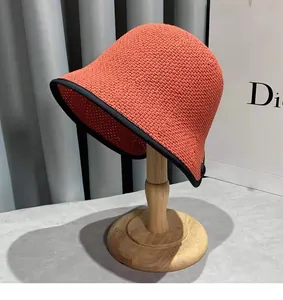 Detailed close-up of a coral crochet bucket hat with black piping on a wooden stand