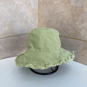 Dettaglio del cappello alla pescatora in tela verde chiaro con bordo sfrangiato