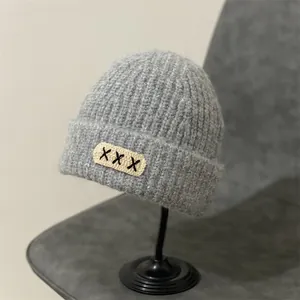 Detail of grey chunky knit beanie with decorative cross-stitch patch and soft mohair texture