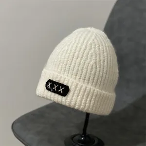 Close-up of ribbed white knit beanie featuring a black patch with white X stitch detail