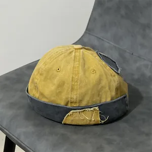 Dettaglio del berretto docker giallo e grigio con toppa vintage e bordi a taglio vivo