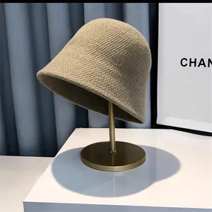 Detailed close-up of khaki knitted bucket hat texture on a golden display stand