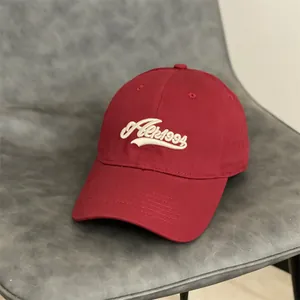 Casquette vintage rouge foncé en coton avec broderie 3D crème posée sur un fauteuil