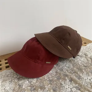 Close-up of burgundy and brown wool bucket hats with gold metal logo plates on white lace