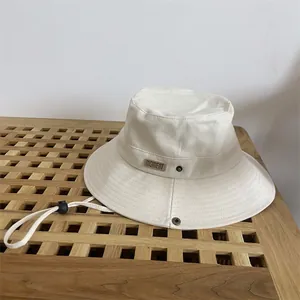 Detail of ivory canvas bucket hat with MOMENT leather patch and windproof drawstring