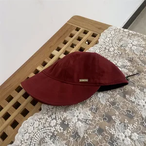 Close-up of burgundy wool cloche hat with metal plaque detail on white lace background