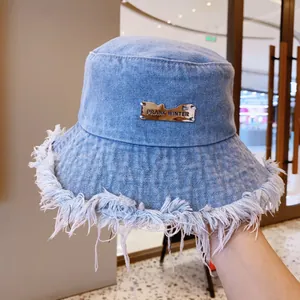 Light blue distressed denim bucket hat with frayed edges and silver metal brand plaque