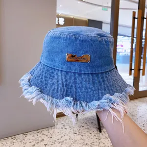 Blue denim bucket hat with frayed tassel edges and a rectangular gold metal plaque