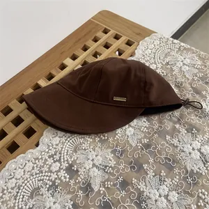 Detail view of deep brown wool fedora hat featuring gold metal side tag and adjustable cord