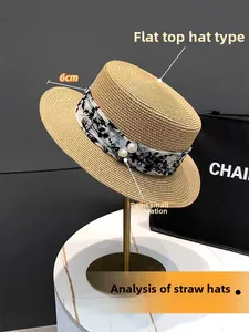 Detail eines flachen Strohhuts mit floralem Chiffonband und Perlenverzierungen