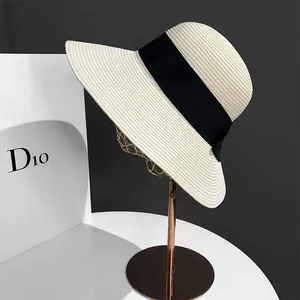 Détail d'un chapeau de paille beige avec ruban noir sur un support en métal doré