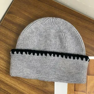 Berretto in maglia grigia con bordo ondulato nero su fondo legno per l'inverno