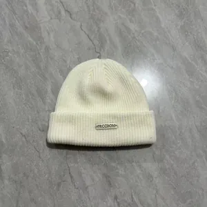 Berretto in maglia bianca con targhetta metallica FRCCDOM su marmo grigio