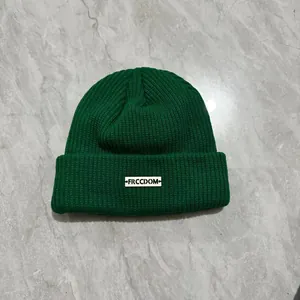 Dettaglio del berretto in maglia verde scuro con patch freedom bianca su trama spessa