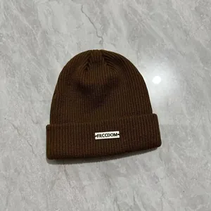 Dettaglio del berretto in maglia a coste color caffè con patch logo Freedom bianca