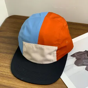 Waterproof five-panel camp cap with multi-color splicing and flat brim on wood table