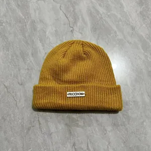 Dettaglio del berretto in maglia giallo zenzero con trama a coste e etichetta intrecciata
