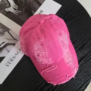 Detailed top view of rose pink distressed baseball cap with ripped edges on black table