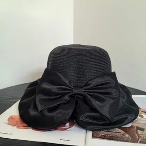 Detail of a black woven straw sun hat with a large satin bow for beach vacations